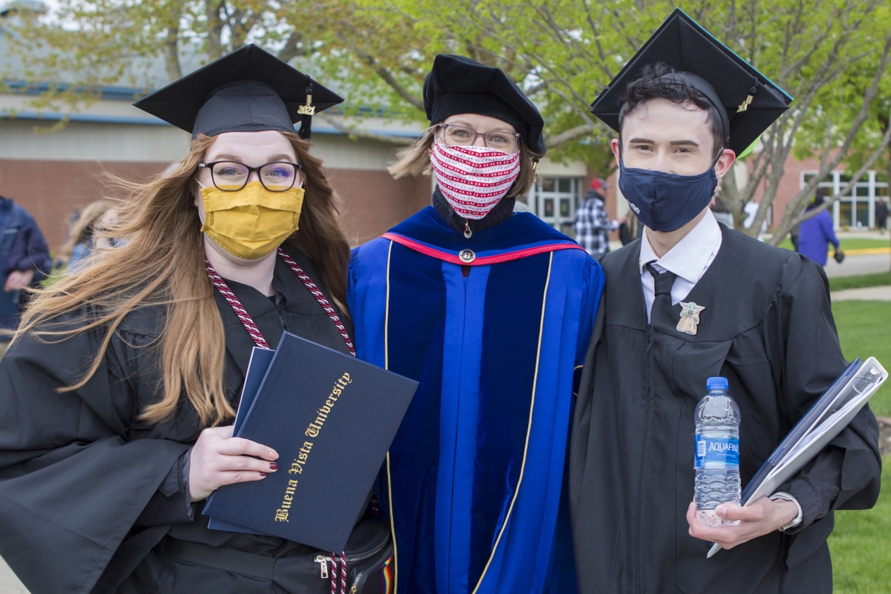 Three people in graduate regalia with arms around each other smiling for the camera.